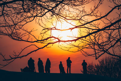 Silhouette people standing by bare tree against sky during sunset