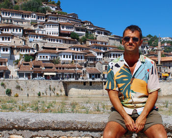 Portrait of mid adult man wearing sunglasses sitting against houses