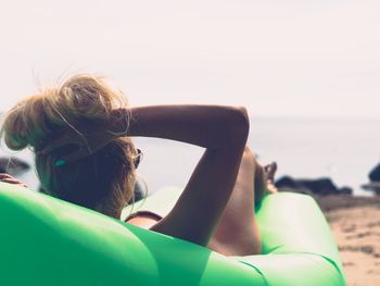 Rear view of sensuous woman relaxing on inflatable chair at beach