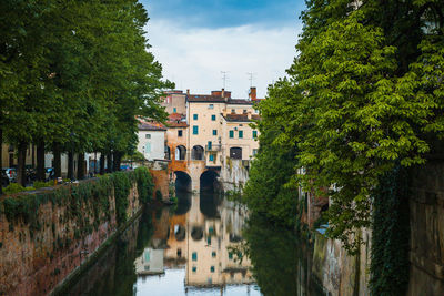 Canal amidst trees and buildings against sky