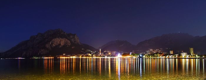 Illuminated lake by mountains against clear blue sky at night