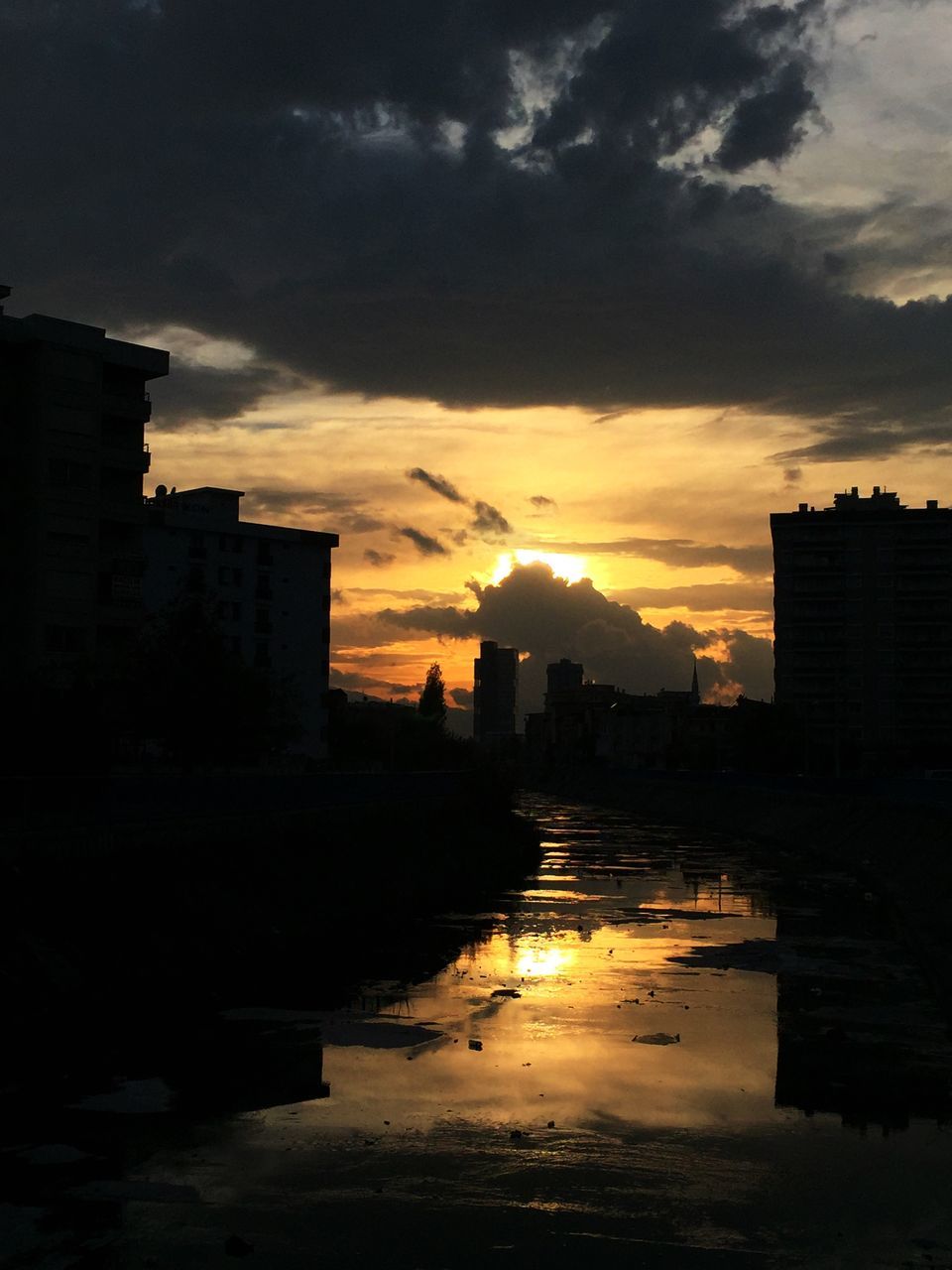 sunset, building exterior, architecture, built structure, sky, silhouette, city, orange color, cloud - sky, water, residential structure, residential building, building, cloudy, dramatic sky, dusk, river, reflection, cloud, house