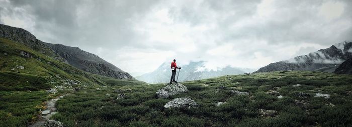 Rear view of man standing on mountain against cloudy sky