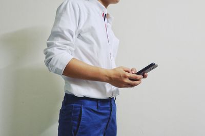 Midsection of man holding mobile phone while standing against wall