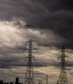 Low angle view of electricity pylon against cloudy sky