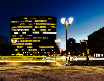 Illuminated street by buildings at night