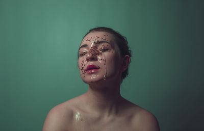 Close-up of shirtless woman with beauty product on face against green background