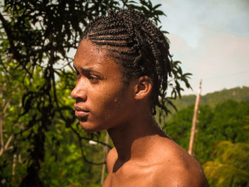 Side view of young man standing against trees