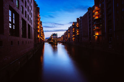 Canal amidst illuminated buildings against sky in city