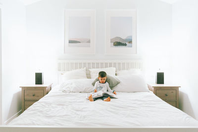 Boy reading picture book while sitting on bed at home