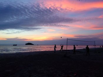 Silhouette people playing on beach against sky during sunset