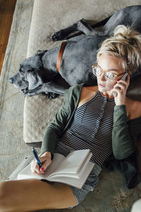 Overhead view of woman talking with diary using smart phone while relaxing on great dane at home