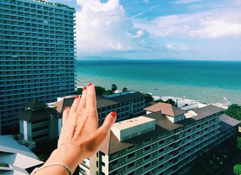 Cropped hand of woman over buildings against sky in city