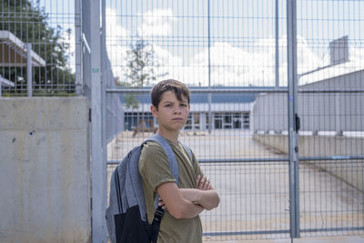 Portrait of confident boy with arms crossed standing against metal gate