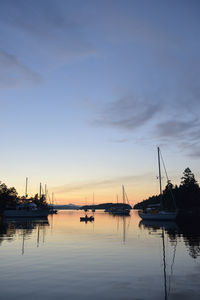 Sailboats moored at harbor against sky during sunset