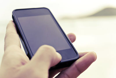 Close-up of hand holding smart phone against sky