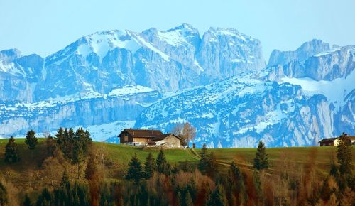 Houses on field against snowcapped mountains during winter