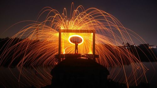 Man spinning wire wool on pier amidst lake at night