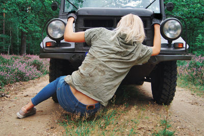 Woman sitting on road by breakdown jeep in forest