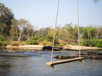 Swing hanging on rope in lake against sky