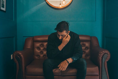 Thoughtful young man looking down while sitting on sofa at home