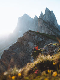 Side view of man sitting on rocky mountains against clear sky