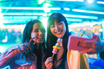 Smiling young women taking selfie while eating candy