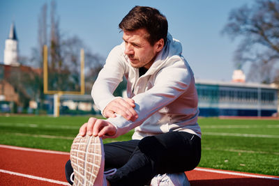Man in sport clothers does a warm-up exercises at stadium track before jogging outdoors