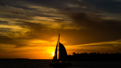 Silhouette sailboat sailing in sea against dramatic sky during sunset