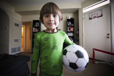 Portrait of boy holding soccer ball while standing at home