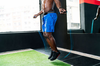 Sweaty african american sportsman with muscular body skipping rope in modern bright fitness center during functional workout