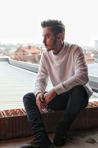 Full length of man sitting on roof against sky