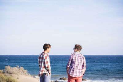 Rear view of friends standing against sea and sky