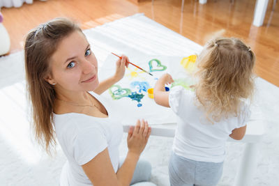 Mother and toddler daughter painting at home. happy creative family with child spending time