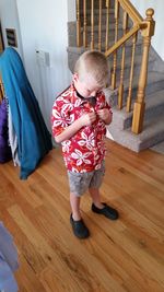 High angle view of boy buttoning shirt while standing on floor at home