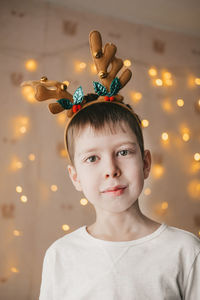 Portrait of a boy in reindeer christmas antlers on the background of an orange garland.