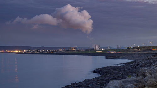 Smoke emitting from factory by sea against sky