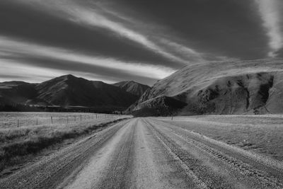 Empty road amidst field against sky