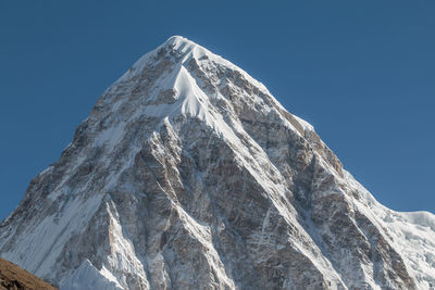 Low angle view of snowcapped mountain against clear blue sky