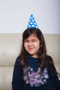 Cute girl wearing party hat while sitting on sofa at home