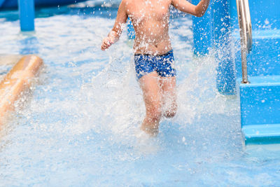 Low section of boy running in water by steps