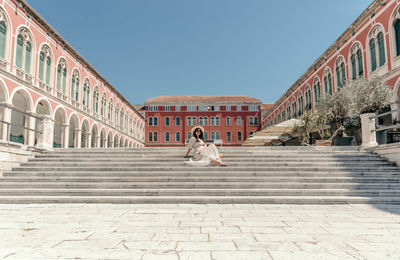 Portrait of beautiful young sitting in square with beautiful architecture in split, croatia