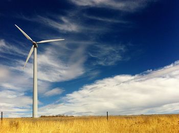 Wind turbine in field under blue sky with clouds