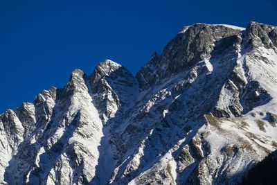 Low angle view of snowcapped mountains against clear blue sky