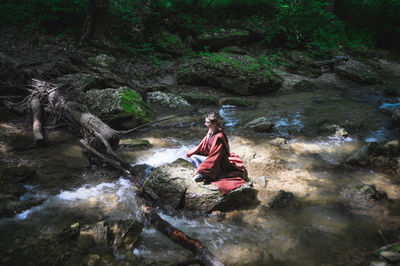 Man sitting on rock by river in forest