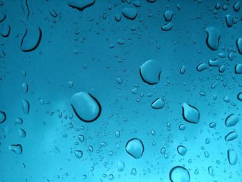 Close-up of waterdrops on glass against blue sky