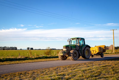 Tractor on road by agricultural field against sky