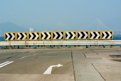 Arrow sign on road in city against sky