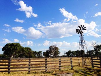 Windmill and trees on field against sky