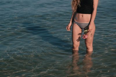 Midsection of woman with flower standing in sea